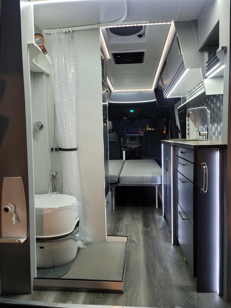 Inside a sleek rv rental: compact wet bath, kitchen with tiled backsplash, bright LED lighting, and convertible seating.