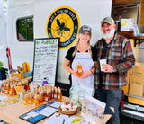 Doc's Healing Hives founders at their honey stand, promoting their veterans' program and RV rental from their mobile shop.
