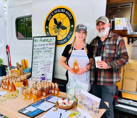 Doc's Healing Hives founders at their honey stand, promoting their veterans' program and RV rental from their mobile shop.