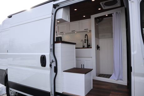 White camper van interior for RV rental. Features a modern kitchen, compact shower, and smart storage solutions.