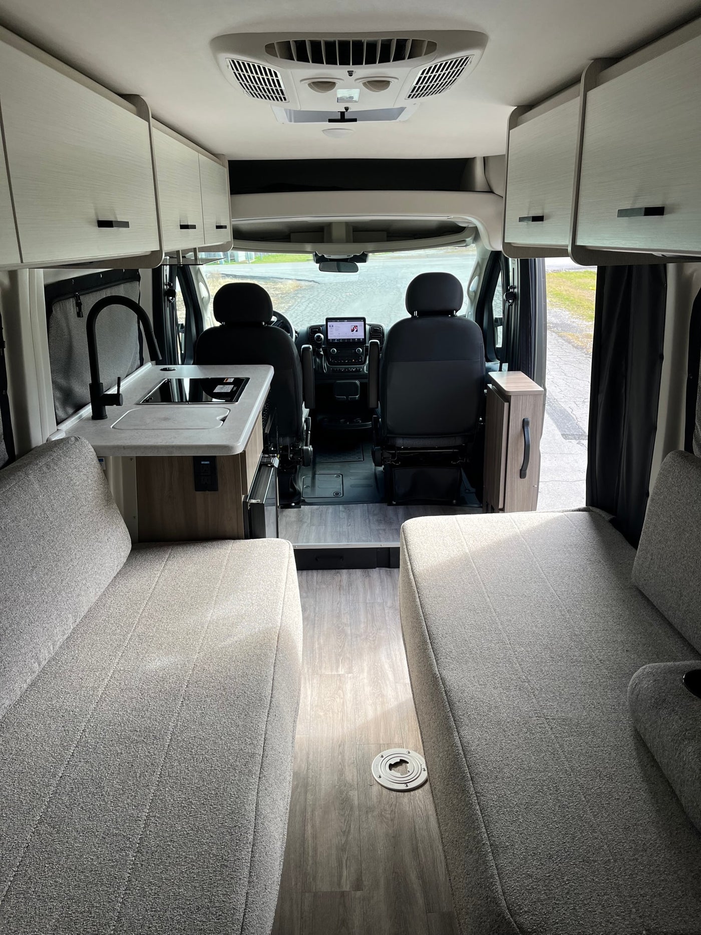 Spacious RV rental interior: modern kitchen, comfortable gray seating/beds, overhead storage, and wood-look flooring. — photo 18