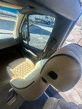 Inside a bright **rv rental**: view of cream quilted captain's seats, looking out at trucks on a sunny lot.
