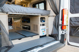 RV rental camper van interior: Rear view of elevated bed, under-bed storage, pull-out trays, and accessible utility panel.