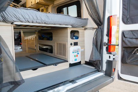 RV rental camper van interior: Rear view of elevated bed, under-bed storage, pull-out trays, and accessible utility panel.
