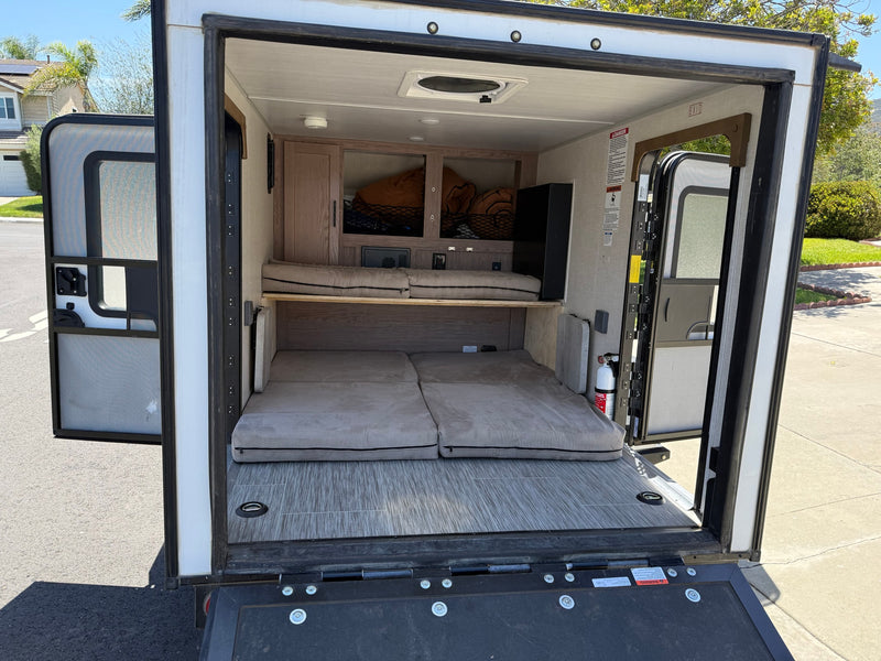 RV rental interior from open rear ramp: showing dual cushioned sleeping areas, overhead storage, and a fire extinguisher. — photo 2
