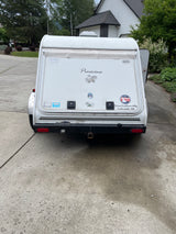 Rear view of a white 'Pinecone' travel trailer, a unique RV rental, parked on a driveway. Manufactured by Three Feathers Mfg.