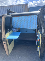 This rv rental features a custom camper van interior: blue palm tree curtain, bed, and a handy fold-down table.
