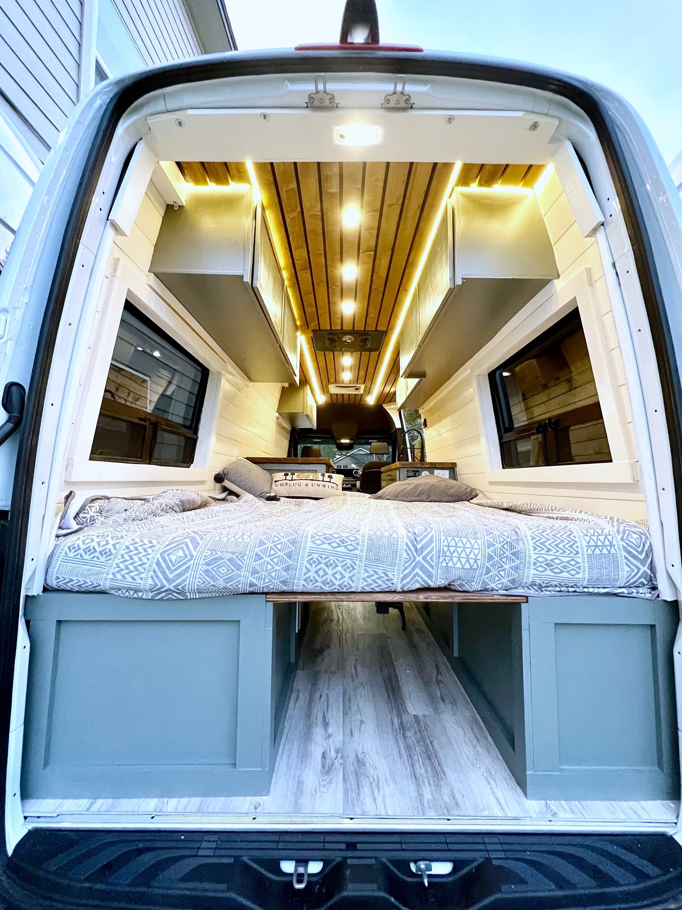 Custom-built RV rental interior: A cozy camper van features a bed, wood ceiling with warm lighting, and storage.
