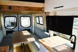 Cozy RV rental interior: dinette with light blue cushions, kitchen with sink, and mounted TV, ready for campervan travel.
