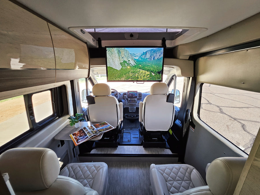 Modern RV rental interior with swiveling front seats, a mounted TV, and cozy rear lounge seating.