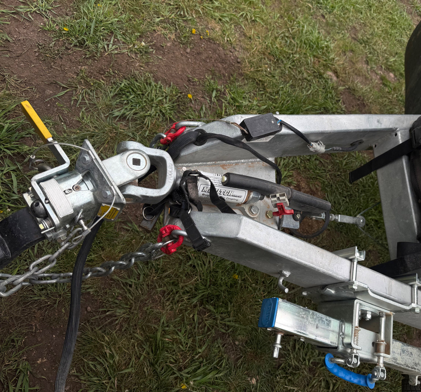 This close-up shows a heavy-duty trailer hitch/coupler assembly with safety chains, wiring, and handbrake, essential for an RV rental.