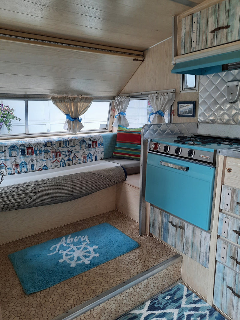 RV rental: Charming interior view with a retro teal stove, wooden cabinets, and cozy nautical-themed decor. — photo 14