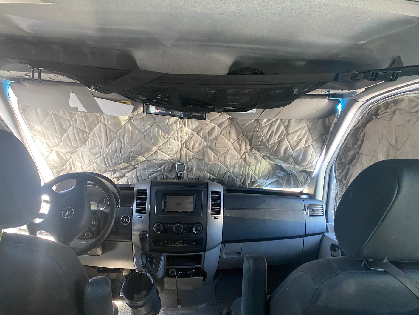 Cozy rv rental interior with quilted windshield covers for privacy and insulation. Overhead net storage and detailed dashboard visible.