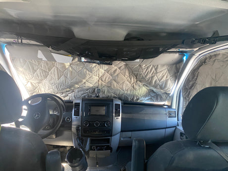 Cozy rv rental interior with quilted windshield covers for privacy and insulation. Overhead net storage and detailed dashboard visible.