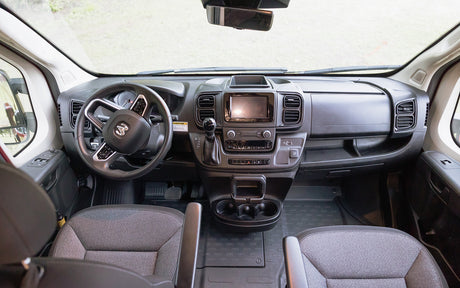 Spacious RV rental interior showing the driver's cockpit, dashboard with touchscreen, and front seats for a comfortable journey.