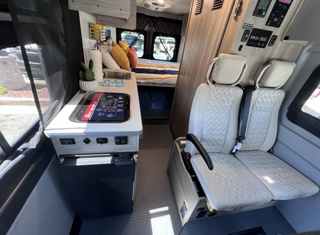 Experience comfort in this rv rental. Features include a compact kitchen, passenger seating, and a rear bed.