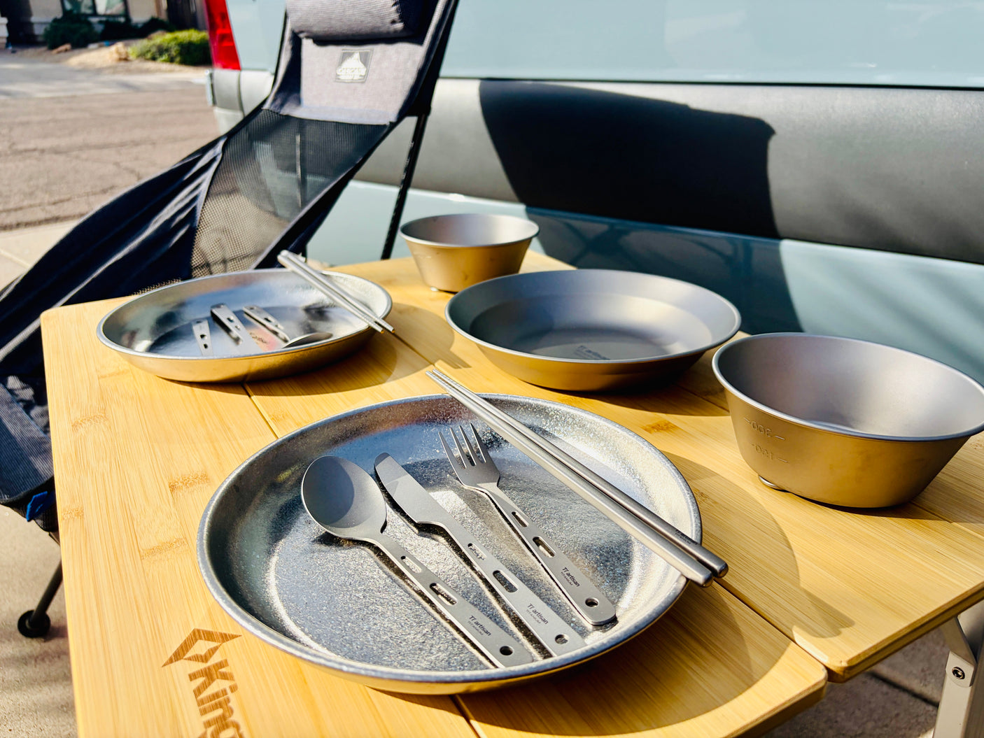 Outdoor dining: Titanium plates, bowls, and cutlery on a bamboo table, set up beside an rv rental.