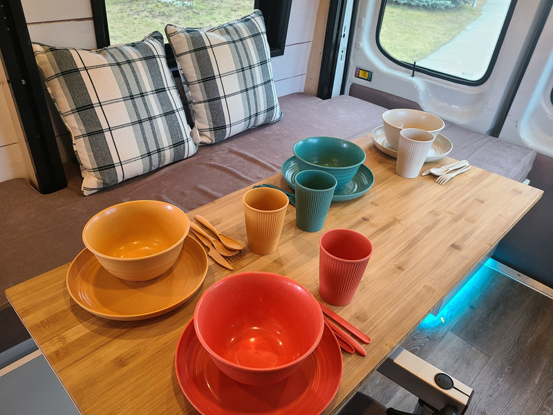 RV rental dining space: a wooden table holds colorful dishware, with plaid pillows and an exterior view visible. — photo 5