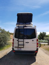 White Mercedes Sprinter camper van, with pop-top tent & ladder, parked for an RV rental adventure.