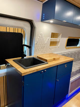 Stylish RV rental interior: blue cabinets, wood counter, black sink, modern backsplash, and cozy seating area.