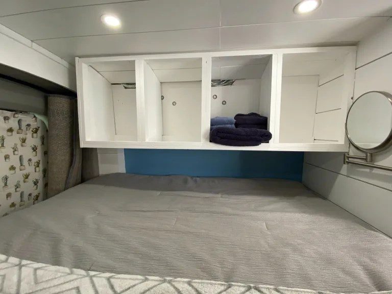 Relax in this RV rental bedroom: comfy bed, white overhead storage shelves, and a wall mirror. — photo 12