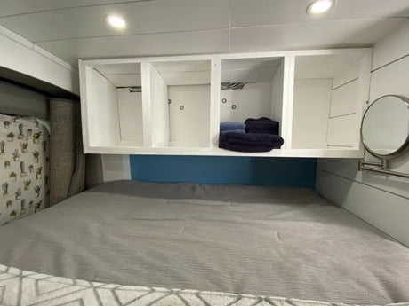 Relax in this RV rental bedroom: comfy bed, white overhead storage shelves, and a wall mirror.