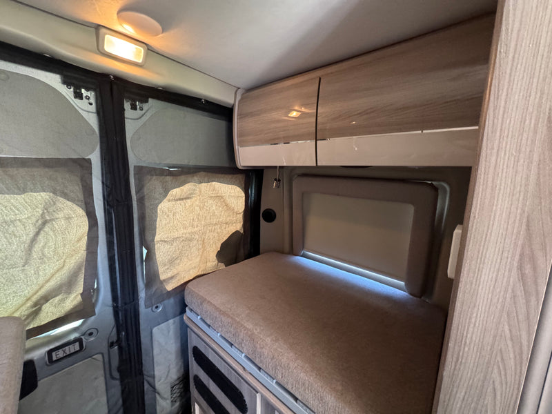 Modern rv rental interior featuring a cushioned bed, sleek overhead storage, and screened windows for comfortable journeys. — photo 10