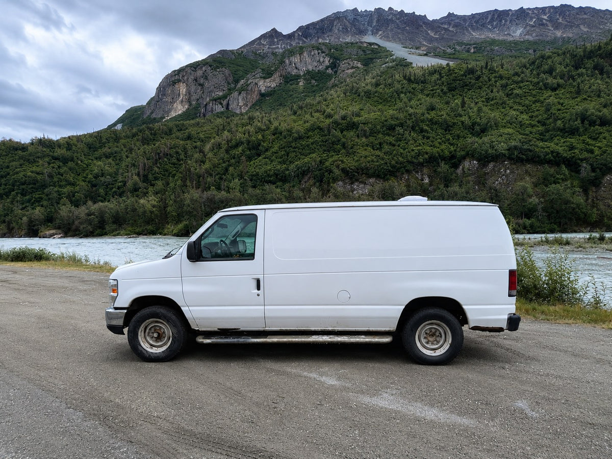  parked roadside with majestic mountains and a vibrant blue sky. Ready for your next road trip adventure.|White camper van parked on a scenic road with majestic mountains & a lush valley. Your next RV rental adventure awaits!|Inside an RV rental van: a cozy bed with pillows — photo 6
