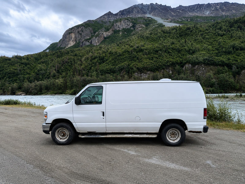  parked roadside with majestic mountains and a vibrant blue sky. Ready for your next road trip adventure.|White camper van parked on a scenic road with majestic mountains & a lush valley. Your next RV rental adventure awaits!|Inside an RV rental van: a cozy bed with pillows — photo 6