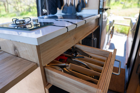 Organized utensil drawer in an RV rental kitchen, featuring a stovetop, modern countertop, and wooden cabinetry.