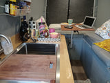 RV rental interior shows a compact living space with a kitchenette, laptop on a table, beverages, and a comfortable sofa.