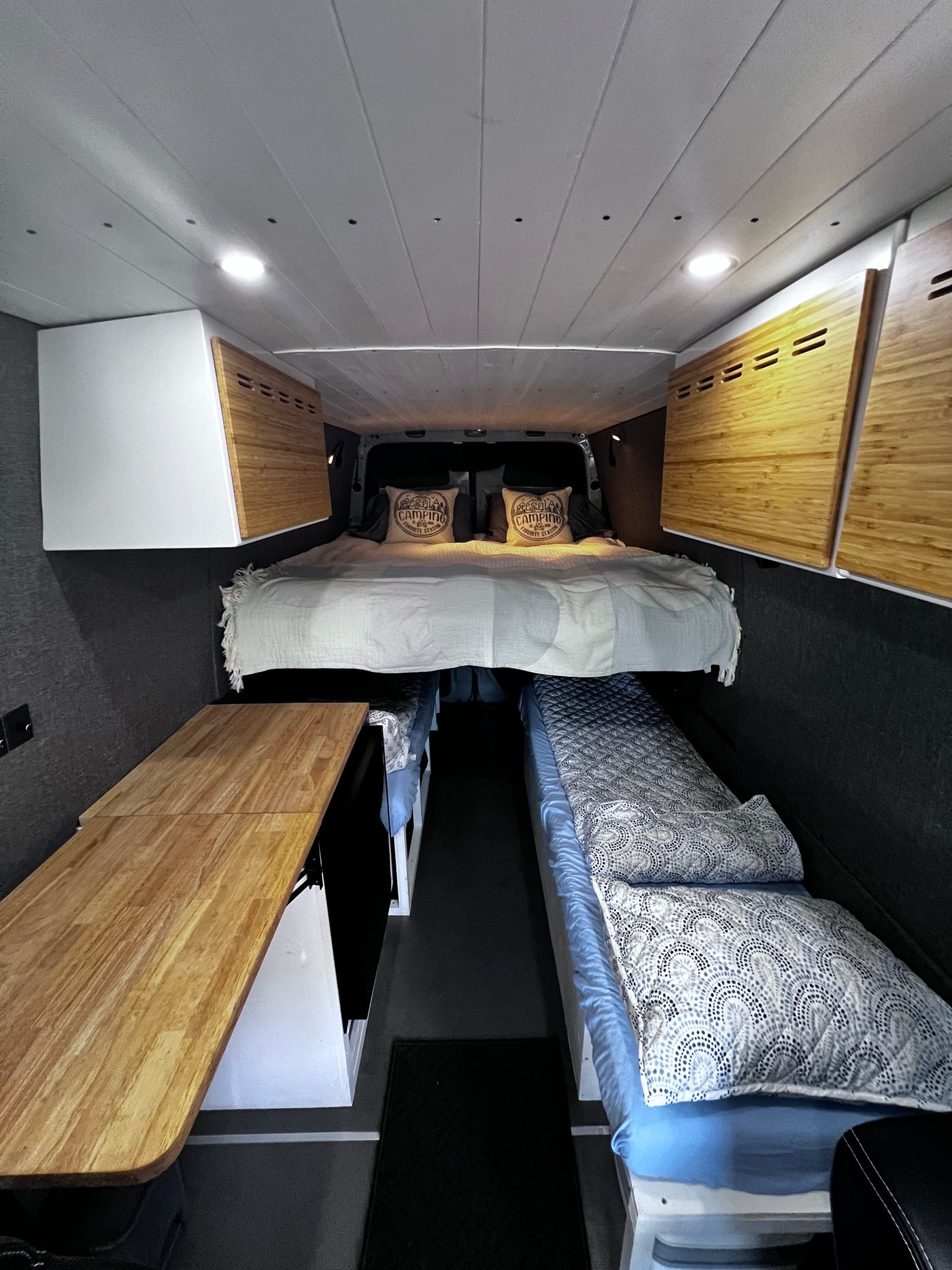 RV rental campervan interior: main bed, two side berths, folding wood table, and overhead storage. — photo 8