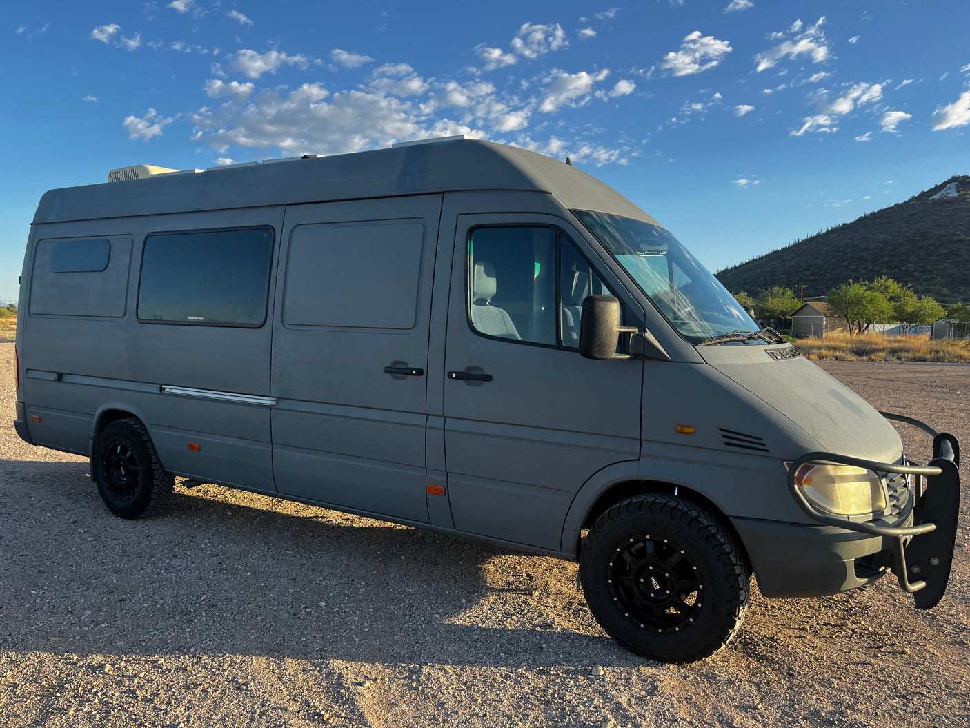 Gray adventure camper van, perfect for RV rental. Parked in a sunny desert landscape under a blue sky.