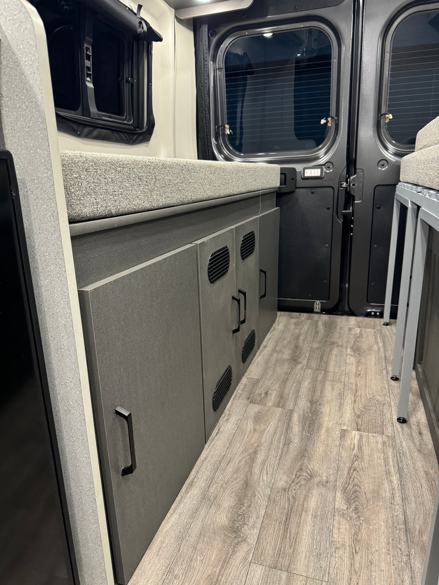 RV rental interior features grey cabinets, wood-look floor, a cushioned bed, and rear van windows.