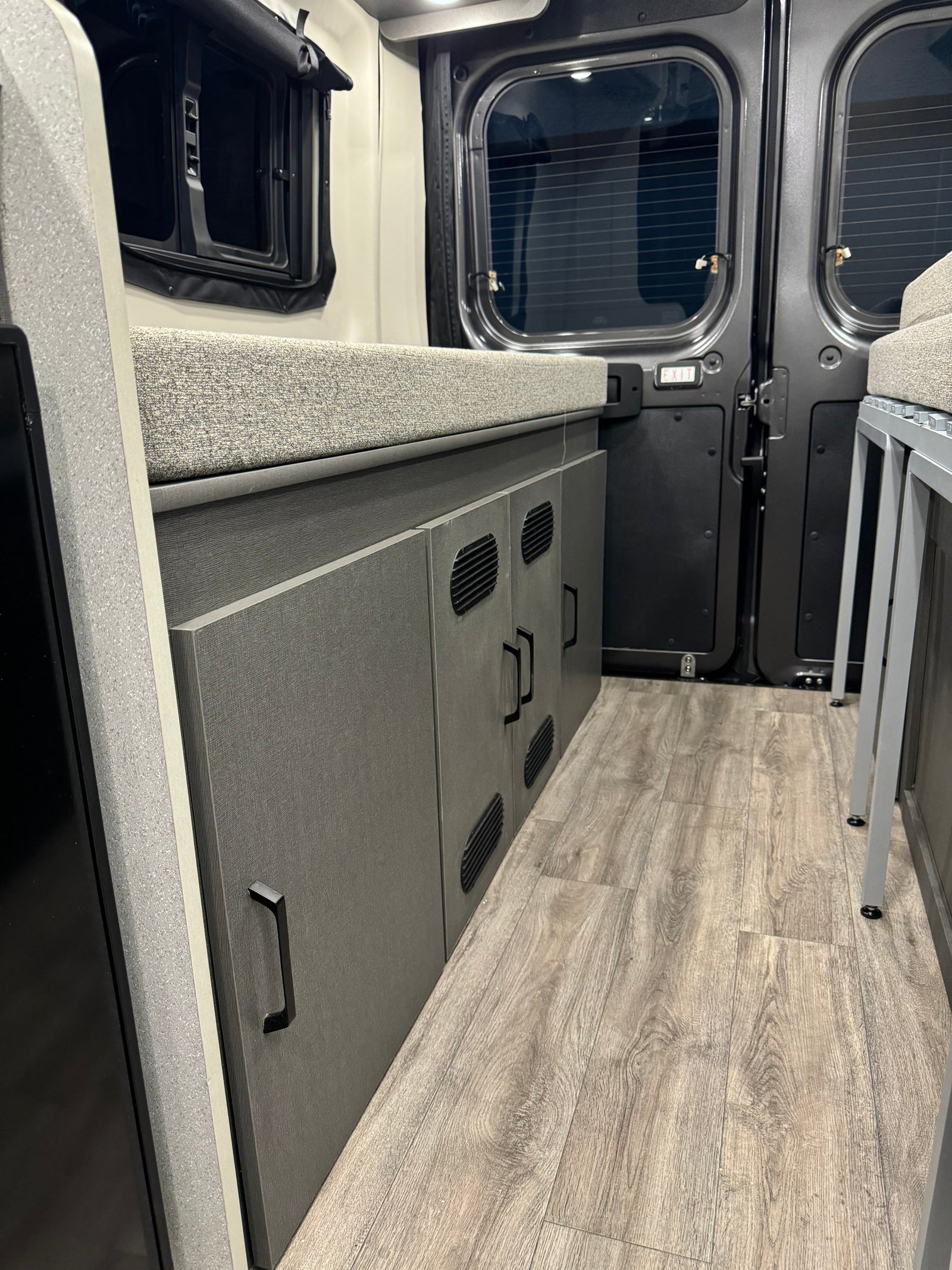 RV rental interior features grey cabinets, wood-look floor, a cushioned bed, and rear van windows.