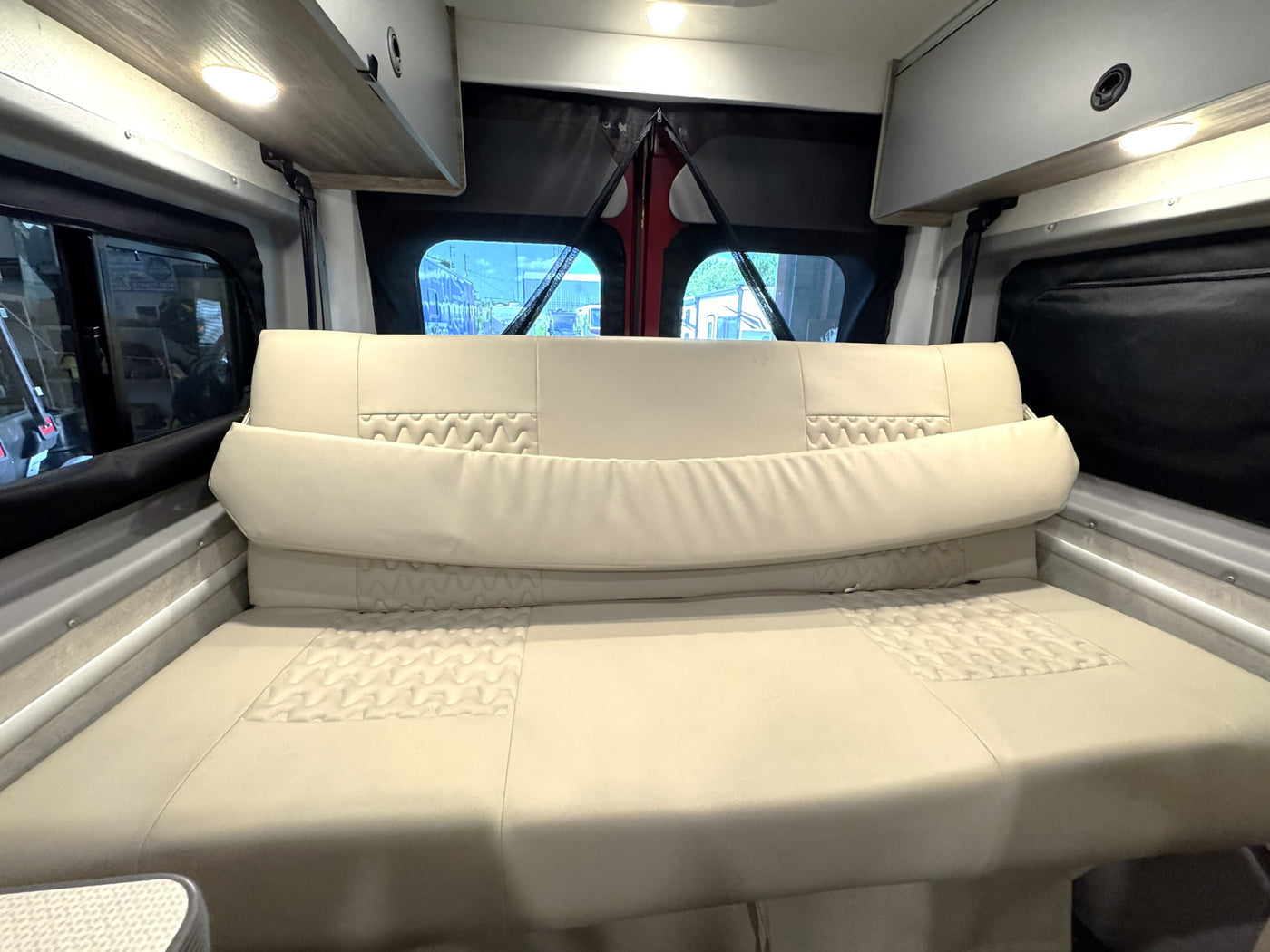 This RV rental interior features a versatile cream-colored modular couch/bed with quilted accents, overhead storage, and rear windows. — photo 20