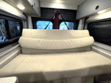 This RV rental interior features a versatile cream-colored modular couch/bed with quilted accents, overhead storage, and rear windows.