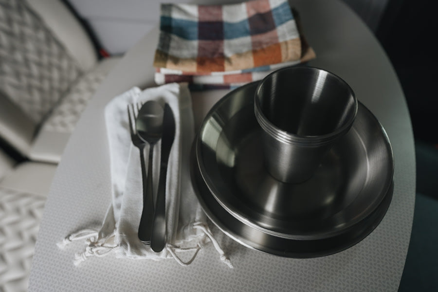 Essential camping gear for your RV rental: stainless steel plates, cup, and silverware set on a patterned table.
