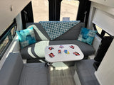 Cozy RV rental interior showing a U-shaped lounge with a table, UNO game cards, and blue pillows.