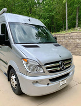 A silver Mercedes-Benz Sprinter camper van, ideal for rv rental, parked on a sunny day with green trees in the background.