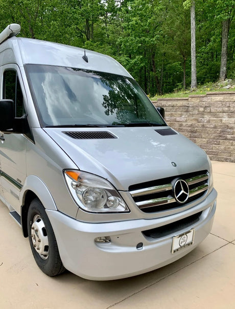 A silver Mercedes-Benz Sprinter camper van, ideal for rv rental, parked on a sunny day with green trees in the background.