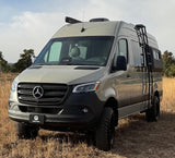 Geotrek Mercedes Sprinter rv rental: tan adventure van with roof rack, ladder, and off-road tires. Ready for exploration.