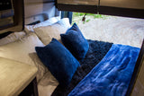 Cozy RV rental bedroom with white sheets, plush blue pillows & blanket, plus an outdoor view.