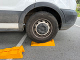 RV rental van parked with its dirty wheel on yellow leveling blocks, with another block nearby, ensuring a stable campsite setup.