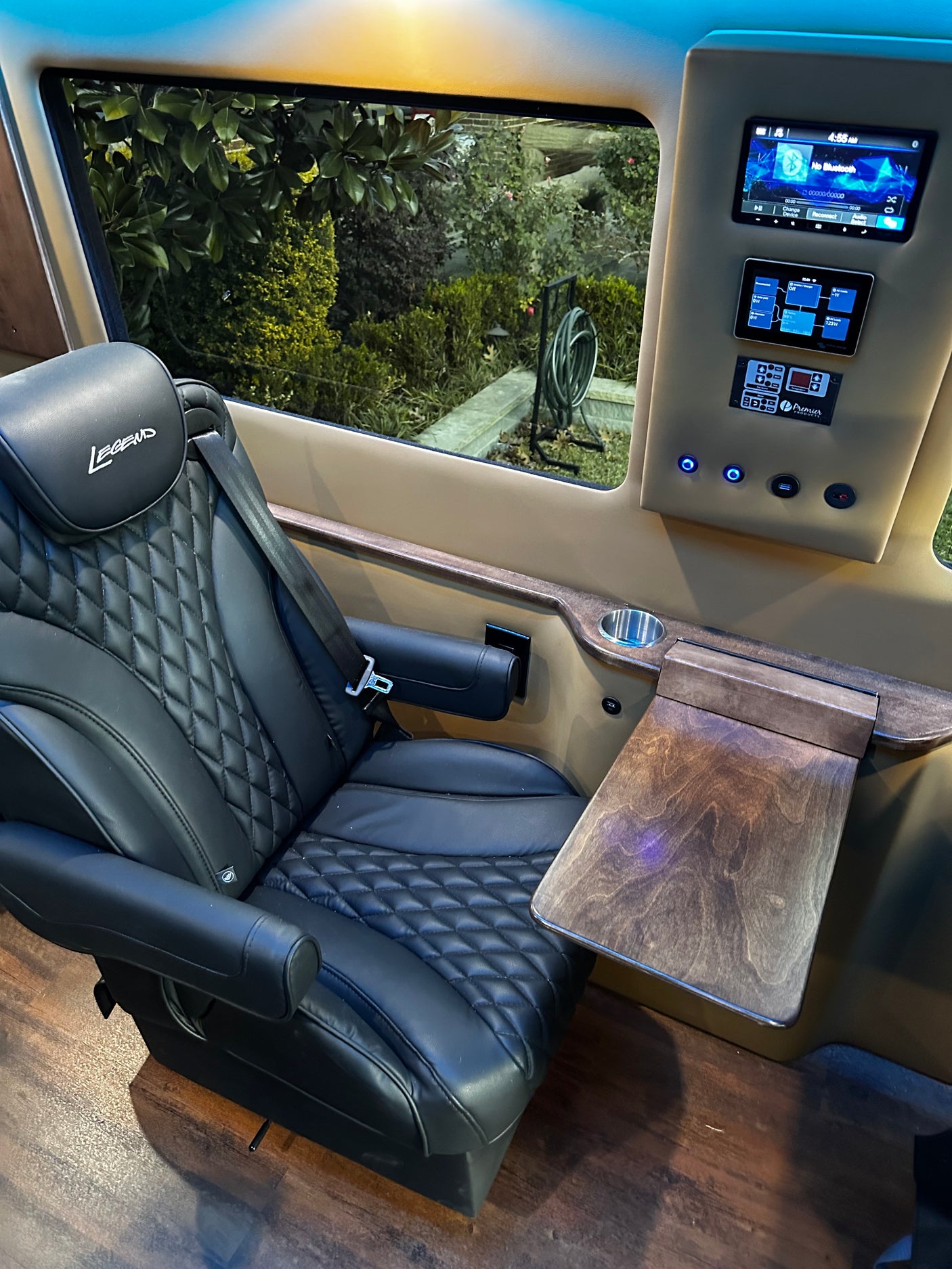 Upscale RV rental interior with a black quilted Legend captain's chair, wood pull-out table, and digital control panel.