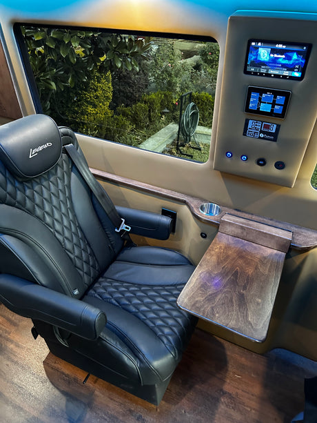Upscale RV rental interior with a black quilted Legend captain's chair, wood pull-out table, and digital control panel.