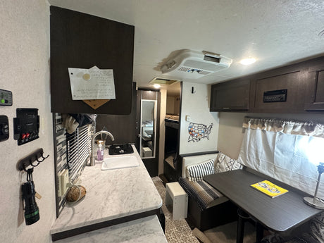 This RV rental interior features a compact kitchen, dining area, and bunk beds. Cozy space for travel adventures.