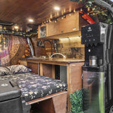 Cozy camper van RV rental interior: a comfy bed with floral mattress, compact wood kitchenette, sink, and water dispenser.