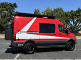 Vibrant red & white Storyteller Overland camper van ready for your next rv rental adventure. Parked outdoors with all-terrain tires.