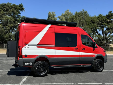 Vibrant red & white Storyteller Overland camper van ready for your next rv rental adventure. Parked outdoors with all-terrain tires.